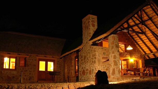 A stone building with a large chimney, wooden doors, and a covered outdoor seating area.