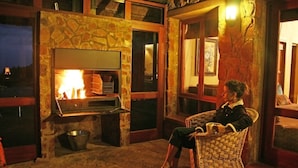 A stone fireplace with a fire, a wicker chair, and a window with a view.