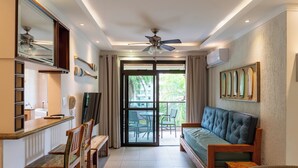 Ein modernes Wohnzimmer mit einer Couch, einem Esstisch, Stühlen, einem Deckenventilator und Blick durch eine Glastür auf einen Außenbereich.