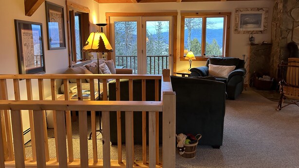 A cozy living room with a wooden ceiling, a fireplace, and a view of trees through large windows. - On Mountain Home, Spectacular Mountain Views, Ski to the Door (Carrabassett Valley)