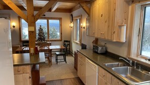 A kitchen with wooden cabinets, a granite countertop, a built-in dishwasher, and a window with a view of snow-covered trees. - On Mountain Home, Spectacular Mountain Views, Ski to the Door (Carrabassett Valley)