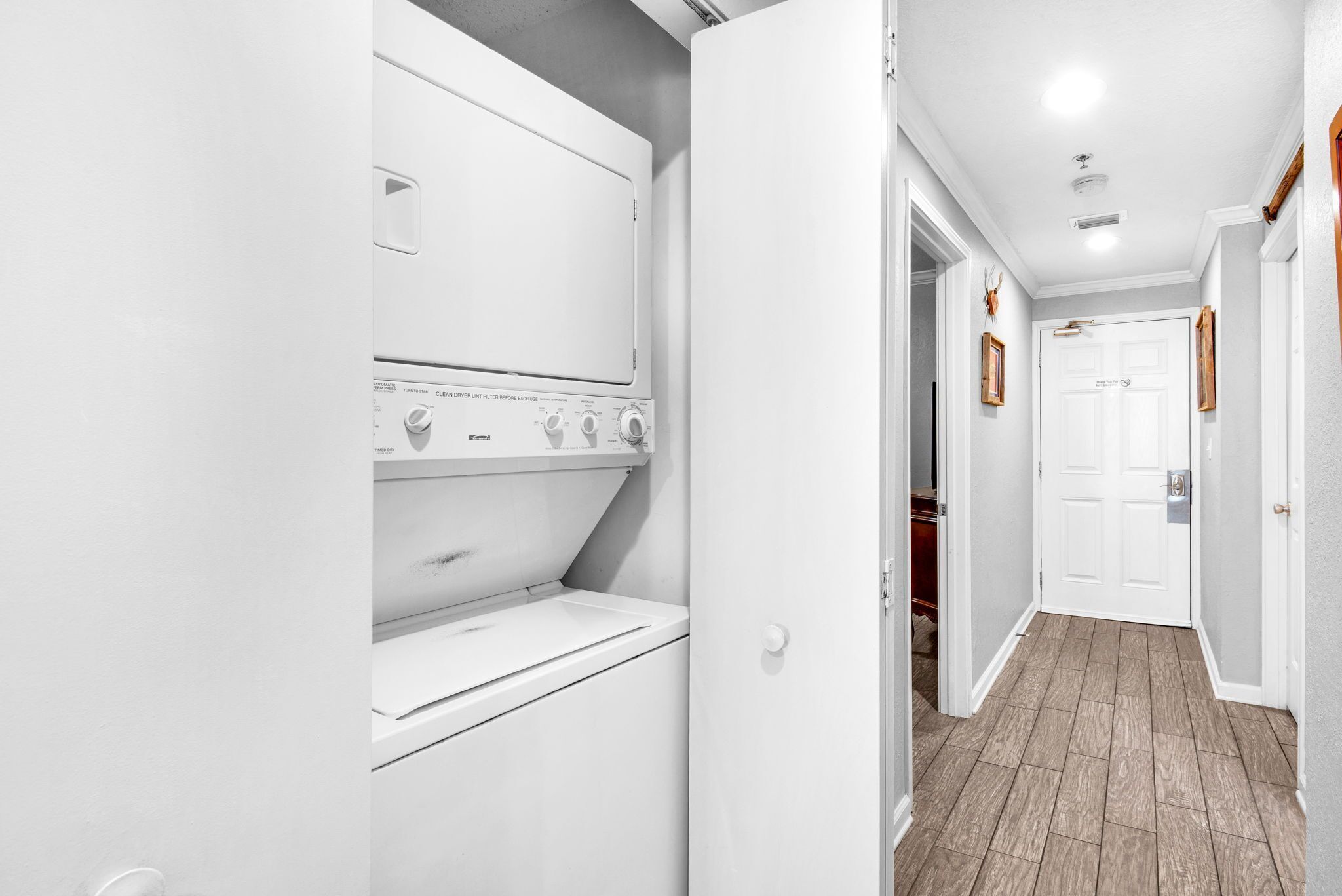 A laundry room with a washer and dryer, a wooden floor, and a white door leading to another room.