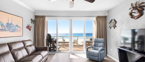 A living room with a brown leather sofa, a blue armchair, a wooden coffee table, a ceiling fan, and a TV on a stand.
