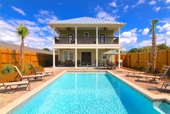 A two-story house with a swimming pool, outdoor furniture, and a wooden fence.