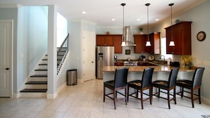 A modern kitchen with a central island, bar stools, stainless steel appliances, and pendant lighting.
