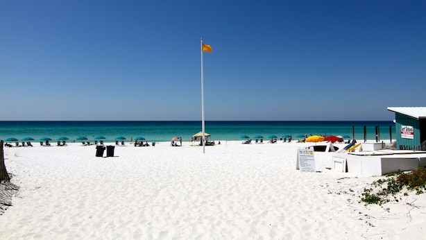 A beach with white sand, a flagpole with an orange flag, and a building labeled "First School".