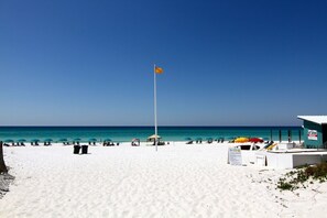 A beach with white sand, a flagpole with an orange flag, and a building labeled "First School".