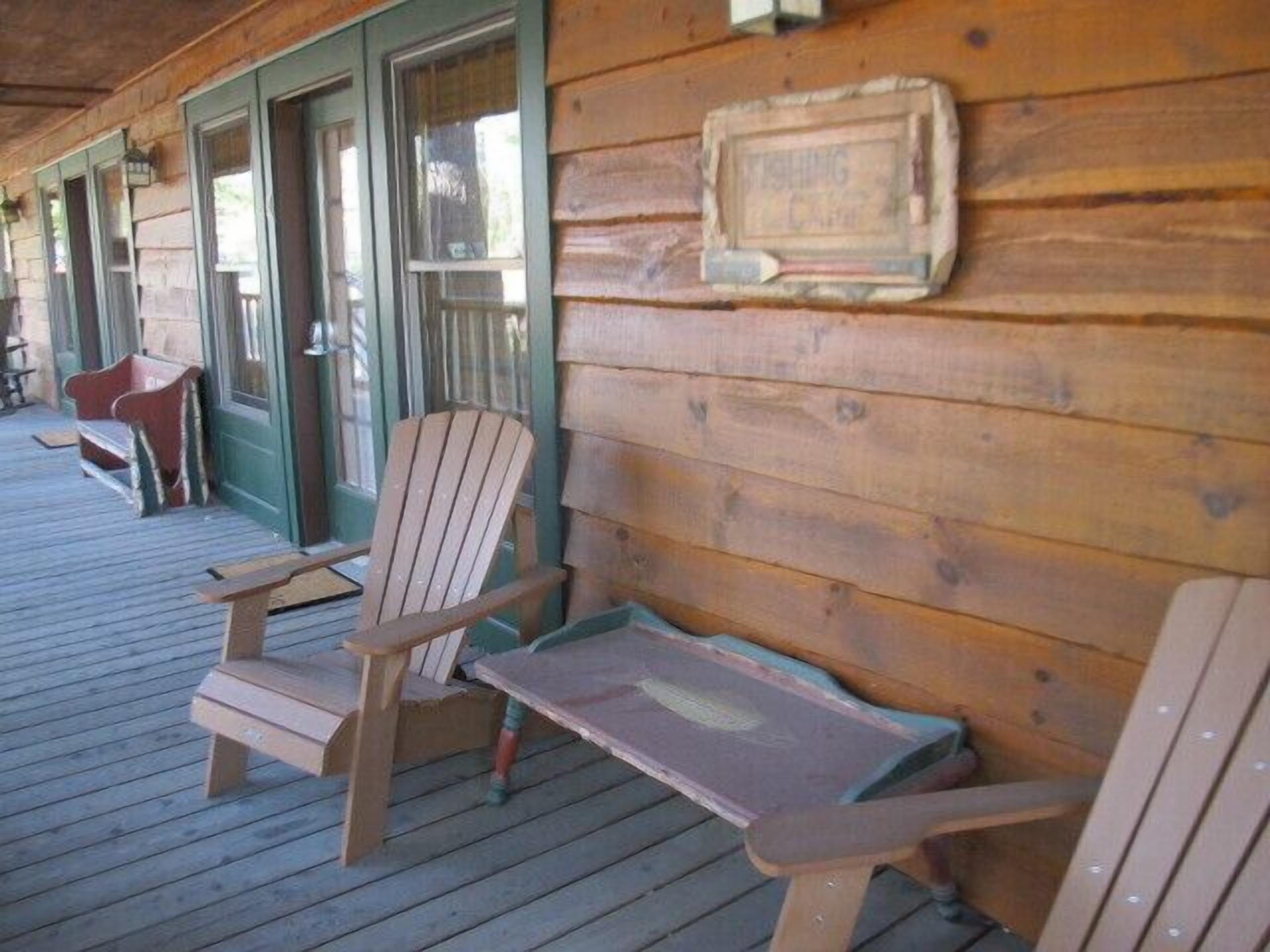 A wooden porch with Adirondack chairs and a small table.