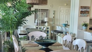 Un coin repas avec une table en verre entourée de chaises en bois, un luminaire suspendu en fibres tressées et une plante en pot.