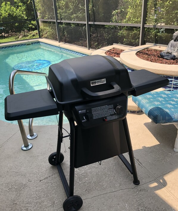 Un barbecue portatif doté d ’une poignée et de boutons de contrôle, placé près d’une piscine dont le bord est recouvert de carreaux et qui est accessible par une échelle en métal.