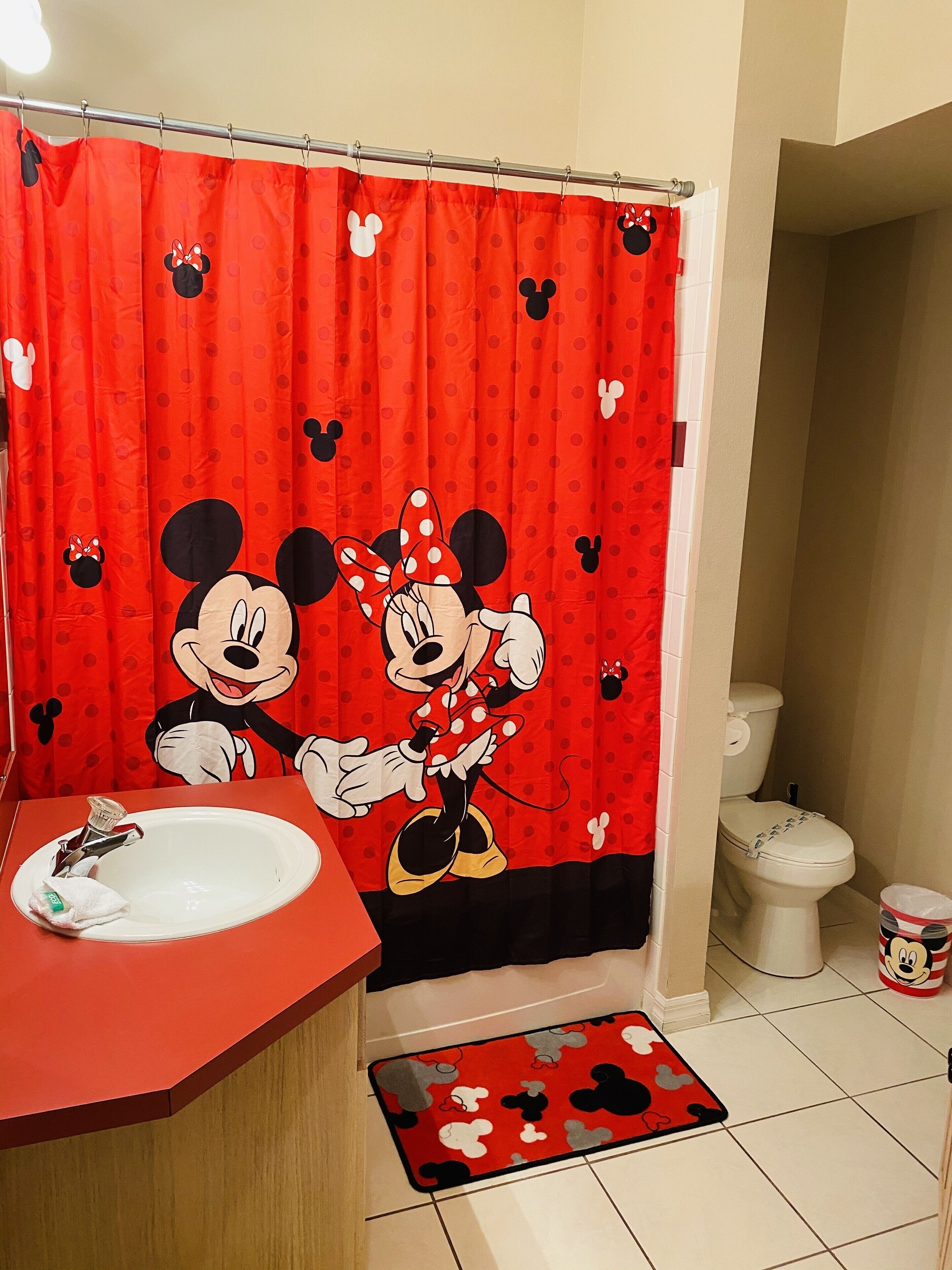 A bathroom with a Mickey Mouse shower curtain, a sink, a toilet, and a Mickey Mouse mat.