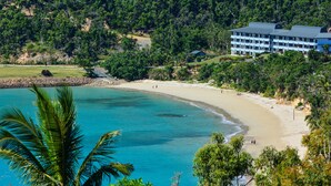 Ein Küstenhotel mit Blick auf den Strand, umgeben von üppiger Vegetation und einem klaren, blauen Meer.
