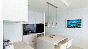 A modern kitchen with white cabinetry, a black stove, and a dining area with a white table and chairs.