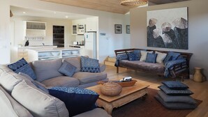 A modern living room with a sofa and a coffee table, a dining area with a kitchen in the background, and a large abstract painting on the wall. - SORRENTO TENNIS RETREAT - 4BR and tennis court, just 5min walk to Sorrento strip (SORRENTO)