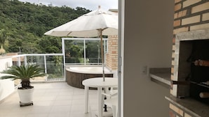 Een balkon met een witte tafel en stoelen, een plant in pot en een grote parasol.