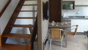 Een moderne keuken met witte kastjes, een houten trap en een eethoek met stoelen.