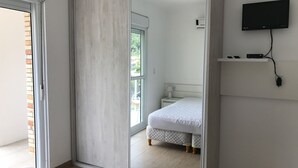 Een slaapkamer met een schuifdeur, een bed, een aan de muur bevestigde televisie en een klein nachtkastje met een lamp.