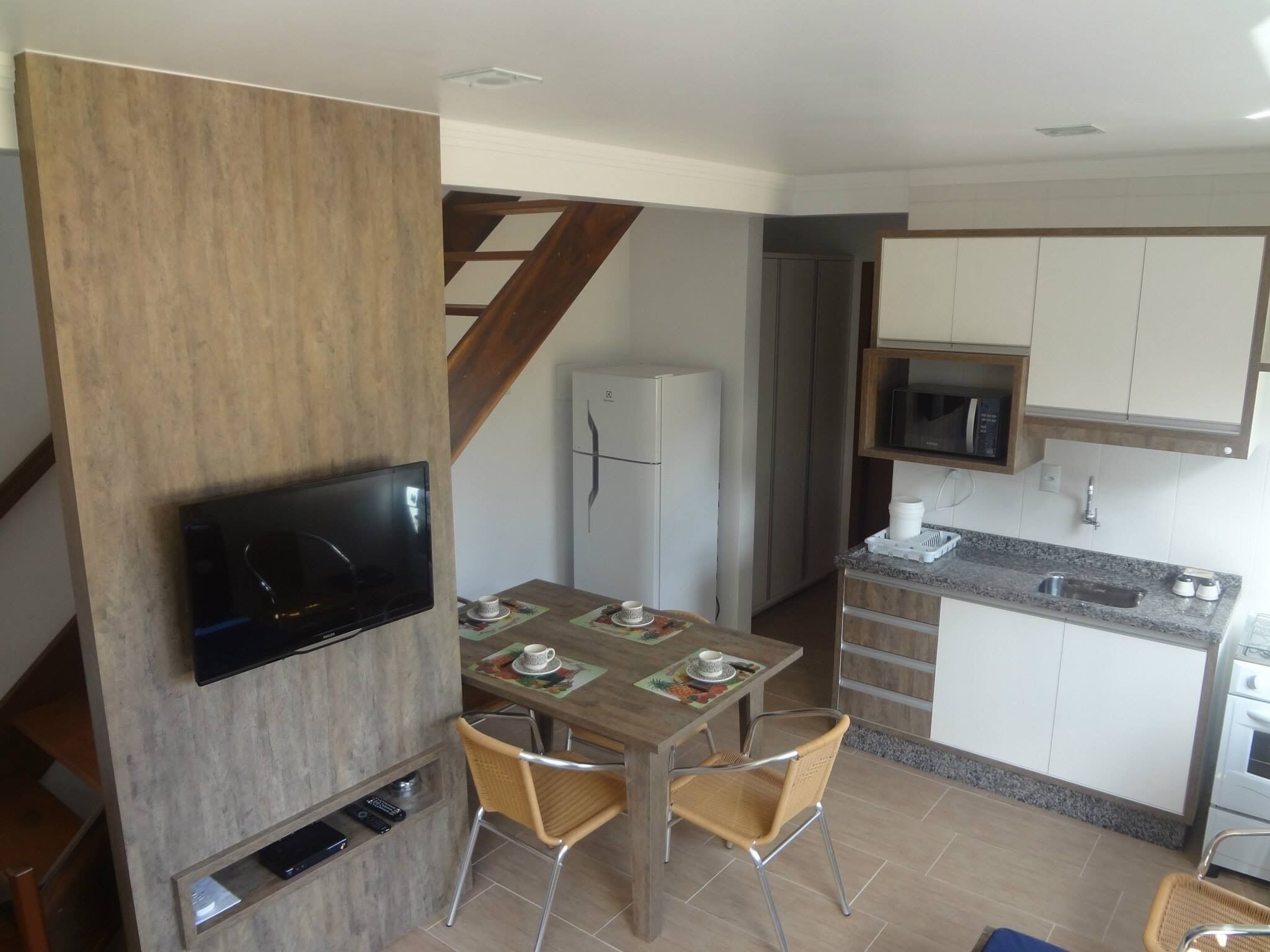 Een kleine keuken met een eethoek, een televisie bevestigd aan een houten paneel, en een magnetron boven het aanrecht.