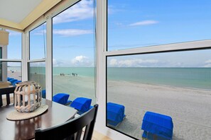 A room with large windows overlooking a beach, a table with chairs, and a woven basket on the table. - Gulf Front Executive level Condominum 2 Master Suites/ 2 full bathrooms (Madeira Beach)