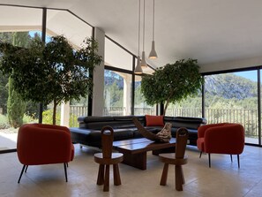 A modern living room with a black leather sofa, red chairs, a wooden coffee table, and hanging pendant lights.