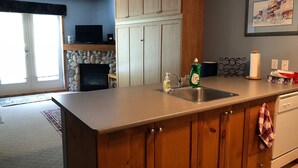 A kitchen with wooden cabinets, a stone fireplace, a sink, and a countertop with a dish soap bottle. - Large balcony, walk out condo on trails - Pet friendly! (Silver Star Mountain)