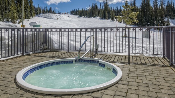 A hot tub with a view of a snowy mountain and a fenced area. - Large balcony, walk out condo on trails - Pet friendly! (Silver Star Mountain)