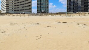 Une plage de sable avec trois immeubles de grande hauteur en arrière-plan.