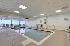 Una piscina interior con paneles de techo transparentes, señales de salida de emergencia y vistas del cielo a través de amplias ventanas.