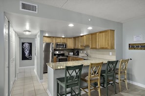 A modern kitchen with granite countertops, stainless steel appliances, wooden cabinets, and a bar area with chairs. - FREE DAILY ACTIVITIES! LINENS INCLUDED*! QUAY - 2BR, 2BA, Ocean View Condo with indoor & outdoor pools & other amenities (Ocean City)