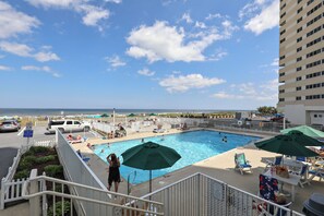 A pool area with a view of the ocean, surrounded by lounge chairs and umbrellas.