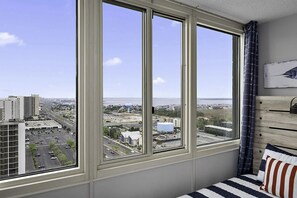Habitación con un amplio ventanal que ofrece vistas a la ciudad, una cama con ropa de cama a rayas y una obra de arte colgada en la pared.