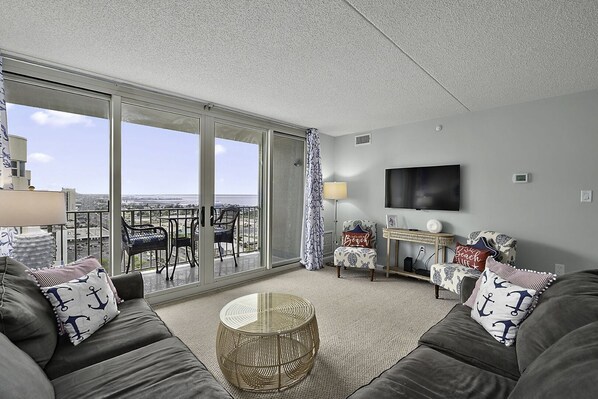 A modern living room with a balcony, a flat-screen TV, and nautical-themed decor.