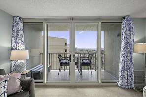 A hotel room with a sliding glass door leading to an outdoor balcony with two chairs and a table.