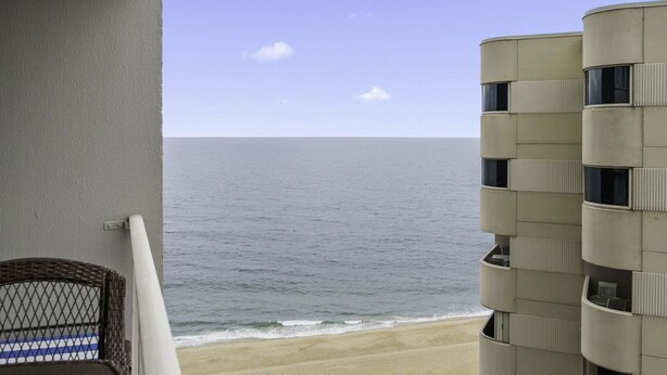 Un balcon donnant sur l’océan, une chaise en osier et un immeuble doté de balcons.
