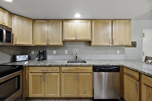 Una cocina con armarios de madera, lavavajillas de acero inoxidable, microondas y cafetera.