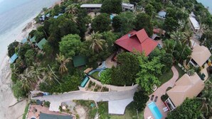 An aerial view of a coastal property with a swimming pool, multiple buildings, and lush greenery.