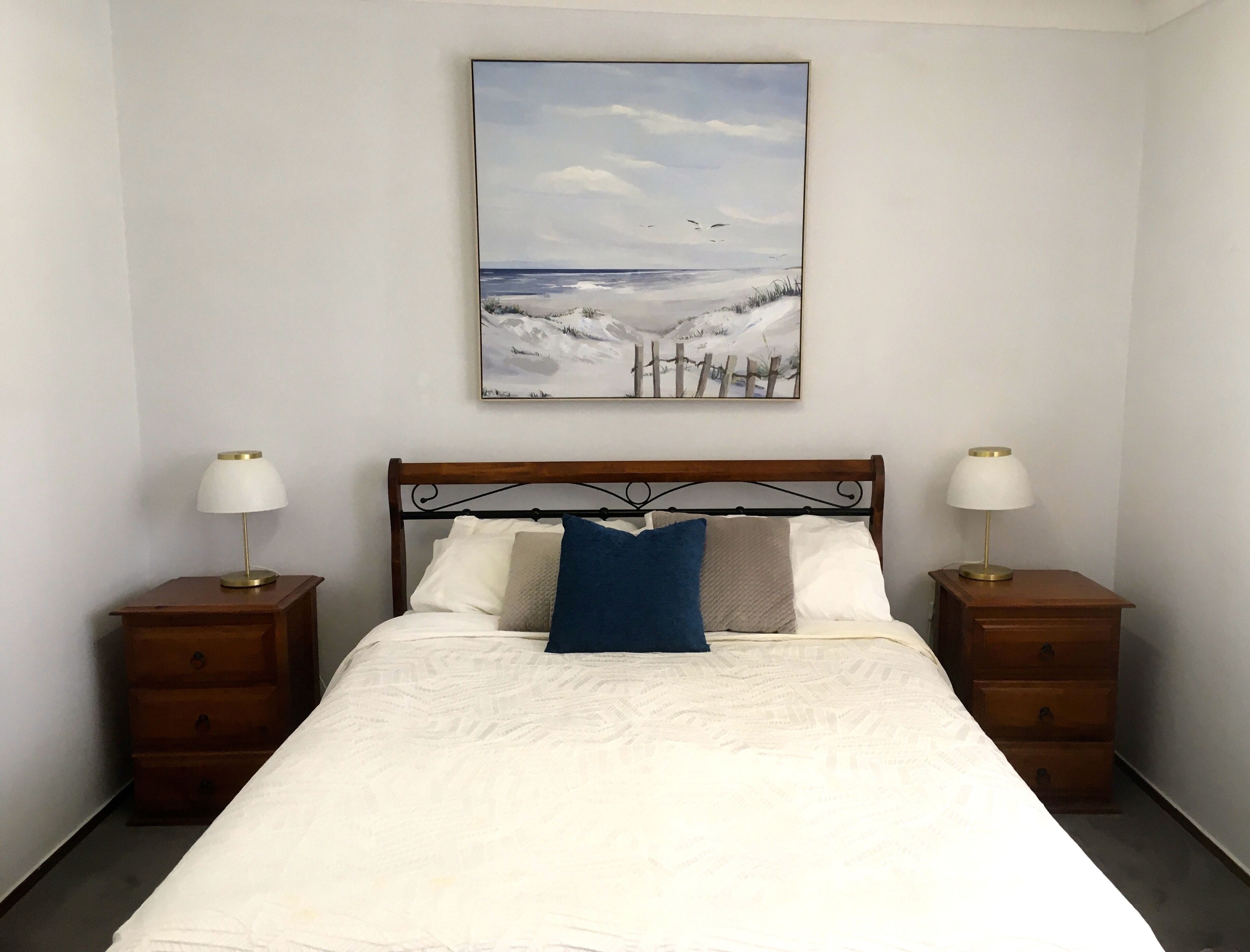 A bedroom with a bed, two bedside tables, and a wall-mounted painting.