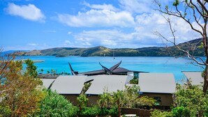 A coastal hotel with modern architecture, a clear view of the sea, and lush greenery.