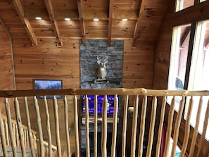 A wooden interior with a stone fireplace, wooden beams, and a television screen displaying a cityscape. - Stairway to Heaven Secluded Cabin, 3 King Suites, Firepit, Hot Tub, Arcade (Gatlinburg)