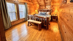 Un dormitorio de cabaña de madera con una cama, un banco, una mesita de noche y un ventilador de techo.