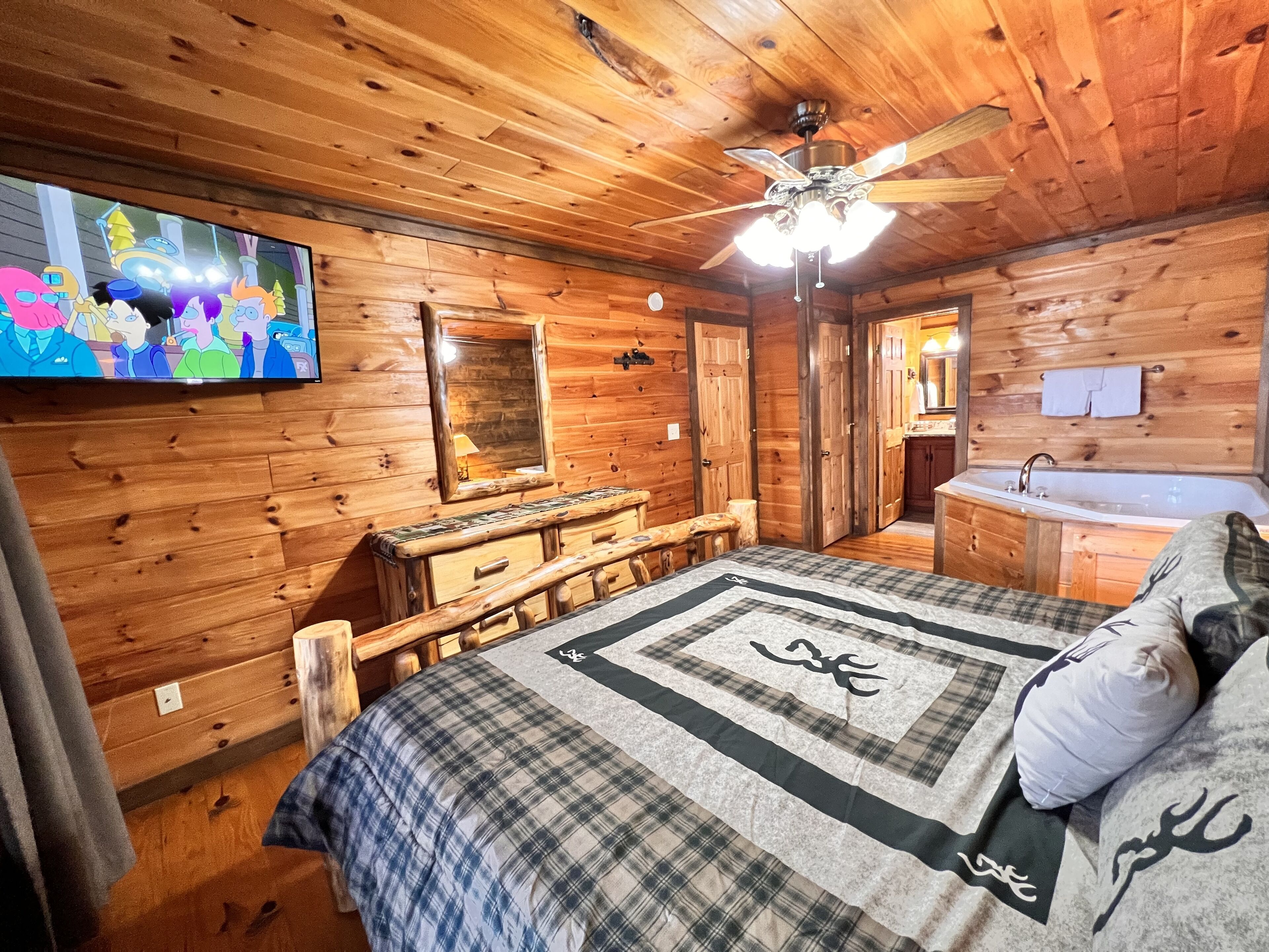 Una habitación tipo cabaña de madera con cama, tocador, televisión y baño con bañera.