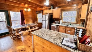 Cocina de cabaña de madera con encimera de granito, armarios de madera, un refrigerador y un comedor con una mesa y bancos.