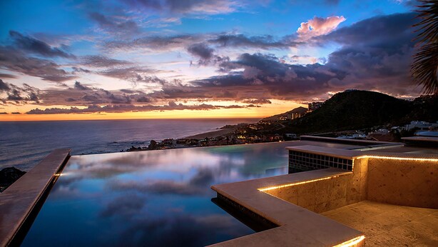 A infinity pool with a view of the ocean and a sunset.
