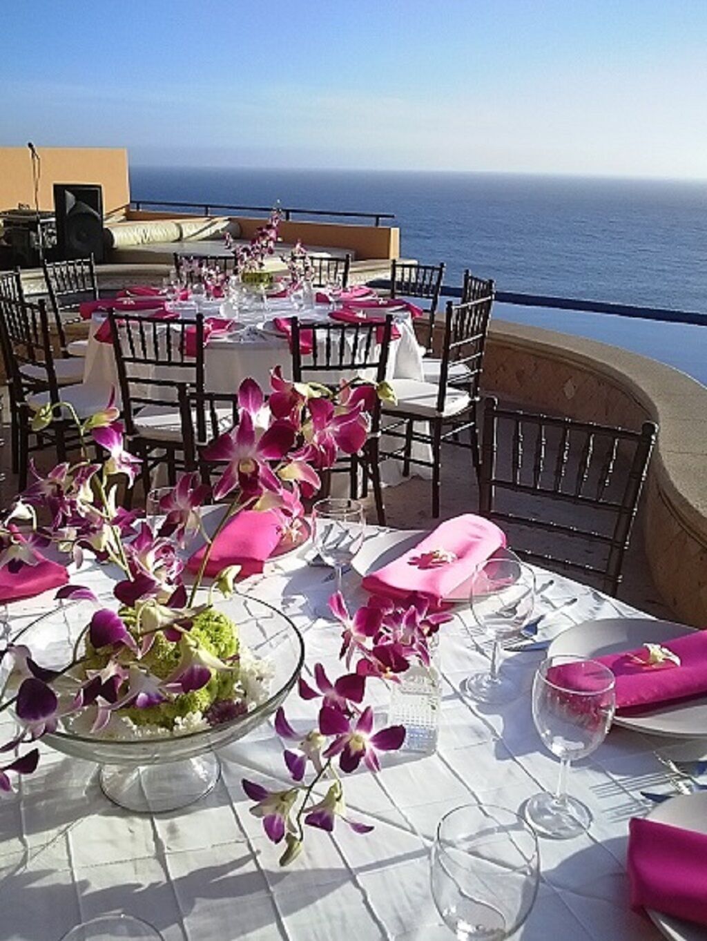 An outdoor dining area with tables set for a meal, overlooking the ocean.