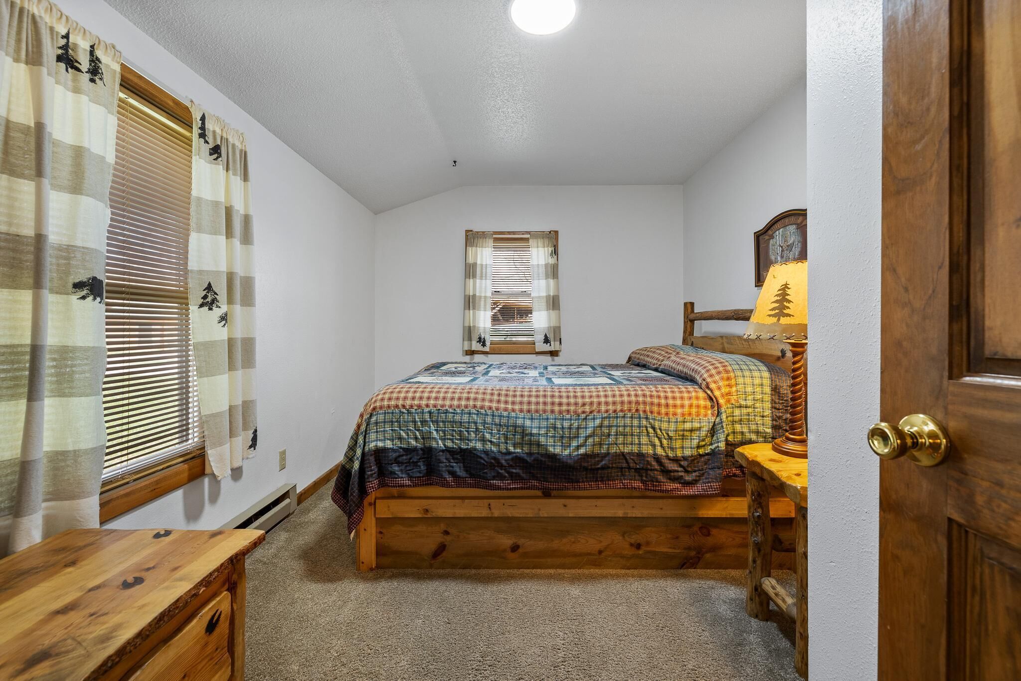 A bedroom with a wooden bed, a nightstand, a lamp, and a window with blinds.