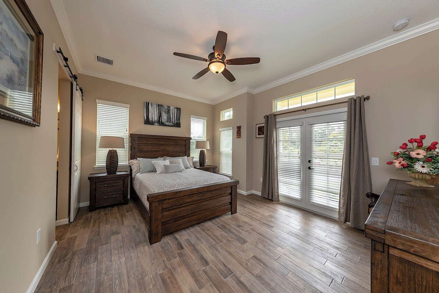 A bedroom with a wooden bed, a ceiling fan, and a view of the outdoors through a sliding glass door.