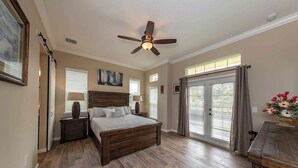 Une chambre à coucher avec un lit en bois, un ventilateur de plafond et une vue sur l’extérieur grâce à une porte-fenêtre coulissante.