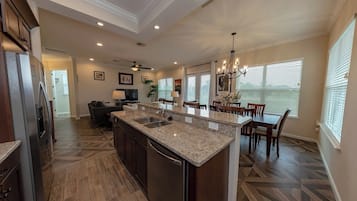 A spacious kitchen with a large island, dark wood flooring, and a dining area with a chandelier.