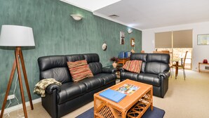 Un salon avec deux canapés en cuir noir, une table basse, une lampe et, au fond, un coin repas.