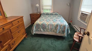 Une chambre à coucher comprenant un lit, une commode, une table de chevet, une lampe et une fenêtre avec des stores.